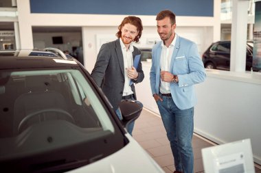 Araba galerisinde hoş bir atmosferde müşteriye yeni bir model sunan bir satıcı. Araba, alışveriş, alışveriş.