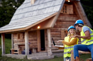 İnşaatçı çift mutlu bir şekilde çalışıyor, kız dizüstü bilgisayara gösteriyor. Ahşap İskelet Çerçeve Binası. İnşaat endüstrisi, gayrimenkul, takım çalışması konsepti.
