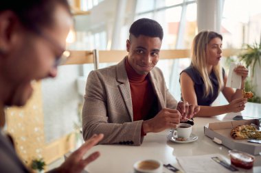 Genç işadamı öğle yemeği molasında şirket binasında hoş bir atmosferde masada otururken iyi vakit geçiriyor ve kahvenin tadını çıkarıyor. İş, insanlar, şirket.