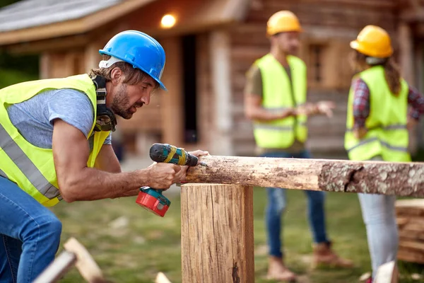 Junger Bauarbeiter Der Mit Einer Bohrmaschine Auf Holzkonstruktion Arbeitet Andere — Stockfoto