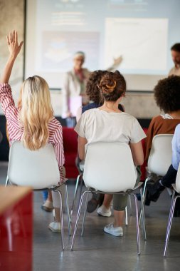 Ofisteki hoş bir atmosferde sunuma katılan genç bir kadın bir soru için elini kaldırıyor.