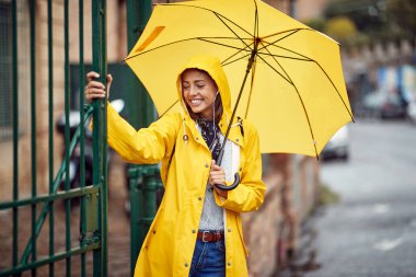 Sarı yağmurluk ve şemsiyeli genç bir kızın yakın çekimi yağmurda huzurlu bir atmosferde şehirde yürümekten keyif alıyor. Yürü, yağmur, şehir