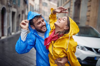 Genç aşık bir çift yağmurlu bir günde neşeli bir atmosferde yürürken yağmurun tadını çıkarıyor. Yürümek, yağmur, şehir, ilişki