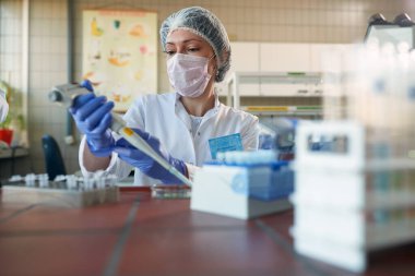 Koruyucu giysiler içindeki genç bir kadın bilim adamı steril bir laboratuvar ortamında pipetle dikkatlice çalışıyor. Bilim, kimya, laboratuvar, insanlar