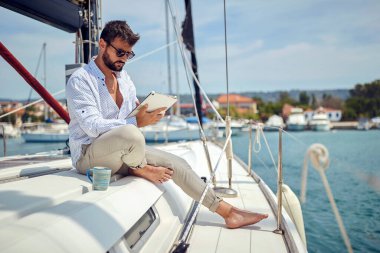Genç bir adam yatta oturup, deniz kıyısında güzel bir günde rıhtımda at sürerken tablet içeriğini seyrediyor. Yaz, deniz, tatil
