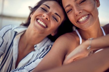 Yatta güneşli bir günde fotoğraf çektirmek için poz veren iki neşeli kadın mankenin yakın çekimi. Yaz, deniz, tatil, arkadaşlık