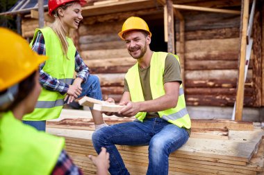 Adam tahta parçasını başka bir inşaat işçisine veriyor. Gülen inşaat işçileri ahşap iskelet iskeleti üzerinde çalışıyorlar. İnşaat endüstrisi, gayrimenkul, takım çalışması konsepti.