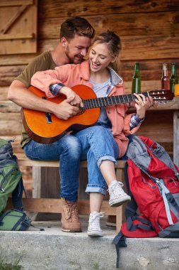 Neşeli, çekici genç çift tatil gününün tadını çıkarıyor ve tahta kulübenin önünde gitar çalıyorlar. Güzel anlardı. Tatil, tatil, birliktelik kavramı.