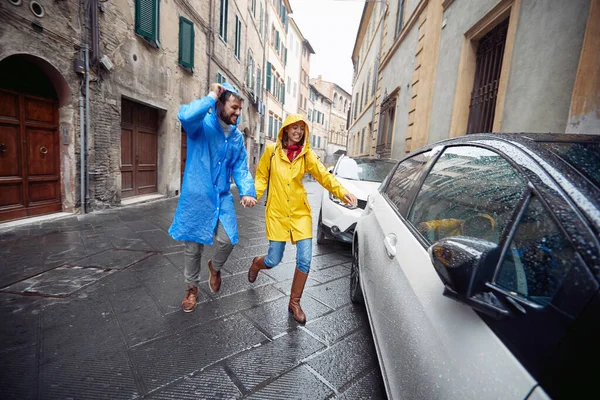 一对恋爱中的年轻夫妇在雨天穿着雨衣在城市里欢快地散步时走到了一辆汽车前 — 图库照片