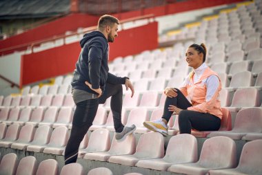 Beyaz sakallı adam ve güzel kadın stadyumda konuşuyor, birbirlerine bakıyor, gülümsüyorlar.