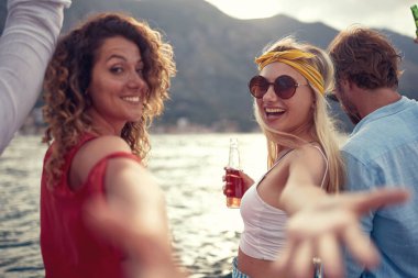 Genç arkadaşlar iskelede oturup konuşuyor, gülüyor ve bira içiyor..