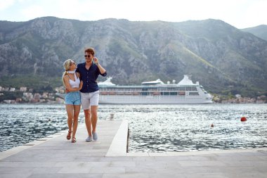 Rıhtımda yürüyen zarif romantik çift. Kruvazör, şehir ve arka planda dağlar. Mutluluk, aşk, tatil, yaşam tarzı konsepti