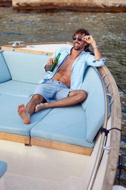 Rahatlamış yakışıklı genç adam yatta eğleniyor, elinde bir bardak birayla. Yaz tatili. Boş zaman, seyahat, yaşam tarzı konsepti.