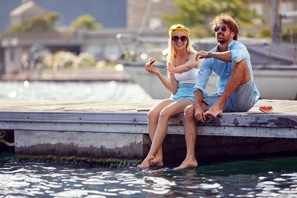 幸せな男と女の子は 湖の桟橋に足をぶら下げて座って スイカを食べる — ストック写真