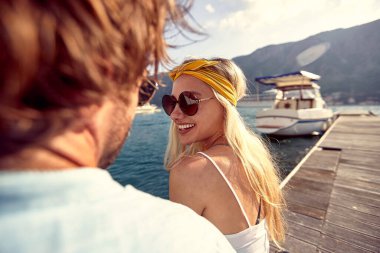 Çekici, neşeli sarışın erkek arkadaşıyla flört ediyor. Ahşap iskelede su kenarında oturan çift. Beraberlik, yaşam tarzı, lüks konsept.