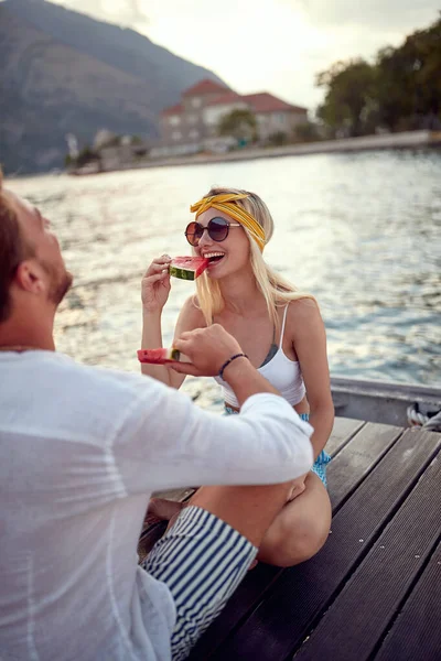 Romantik tatil. Kadın ve erkek göl kıyısında birlikte oturup karpuz yemekten zevk alıyorlar.