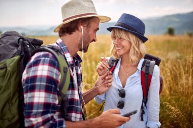 Romantik gülümseyen çift kulaklıklarını doğada paylaşıyor ve müzik dinliyor.