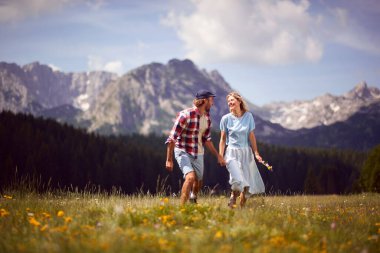 Güneşli bir günde yeşil çayırda yürüyen ve el ele tutuşan gülümseyen çift. Eğlence, birliktelik, yaşam tarzı, doğa konsepti..