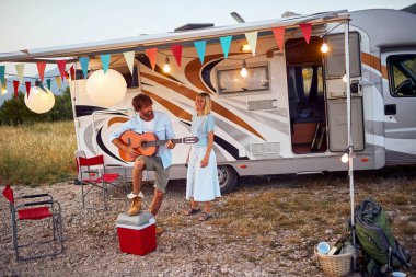 Genç bir çift, doğanın güzel bir gününde kamp alanında bir tatil sırasında müzik çalmaktan zevk alır. İlişki, aşk, kamp, doğa.