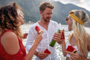 Mutlu insanlar gölde gülerek, karpuz yiyerek ve bira içerek eğleniyorlar..