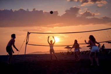 Gün batımında plajda voleybol oynayan bir grup genç arkadaş..
