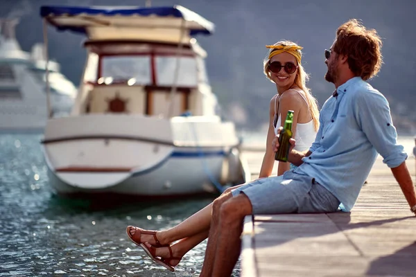 A young couple is sitting on the dock on the seaside and chatting on a beautiful sunny day. Love, relationship, holiday, sea