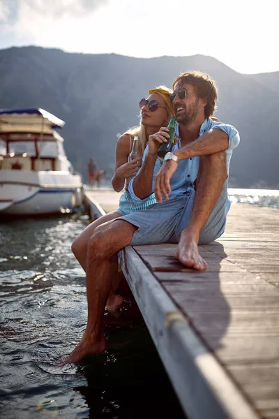 女人靠在她的男朋友 情侣们在水边喝啤酒 坐在木制软垫上 生活方式 奢侈观念 — 图库照片