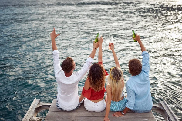 Group Friends Sitting Wooden Jetty Cheering Beer Facing Sea Travel — Stock Photo, Image