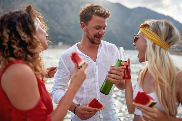 Mutlu insanlar gölde gülerek, karpuz yiyerek ve bira içerek eğleniyorlar..