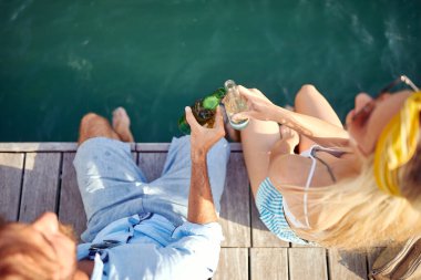 Genç ve mutlu bir çifti kuşbakışı deniz kenarında otururken ve güneşli bir günde içkiyle sohbet ederken görmek. Aşk, ilişki, tatil, deniz