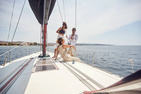 A group of young handsome models is enjoying the sun and the wind while is posing for a photo on the deck of the yacht on a beautiful summer day on the seaside. Summer, sea, vacation, friendship