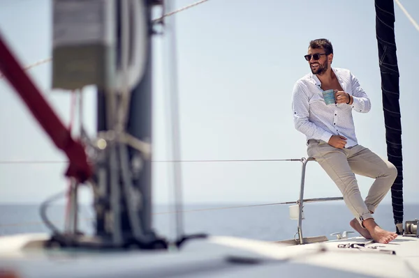 A young handsome barefoot male model is in a good mood while enjoying a photo shooting on a yacht on a beautiful sunny day on the seaside. Summer, sea, vacation