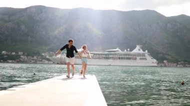 Genç mutlu çift el ele tutuşup, deniz kenarında güvertede koşuyor. Tatil, seyahat, yaz konsepti