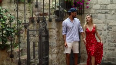 Aşık genç bir çift, deniz kenarında güzel bir günde eski şehrin dar sokaklarında yürürken el ele tutuşuyor. Tatil, deniz kenarı, ilişki, turistler