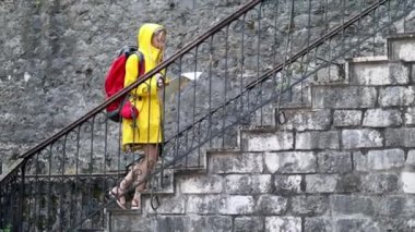 Merdivenlerde elinde harita olan bir kadın. Yağmurlukla şehre doğru yürü. Yaz yağmuru. Seyahat, yaşam tarzı konsepti.