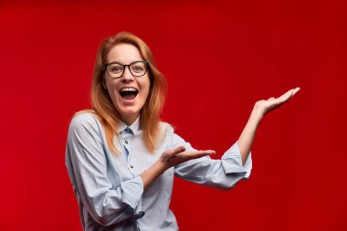 Kırmızı arka planda kızıl saçlı kız bir şeyler sunuyor..