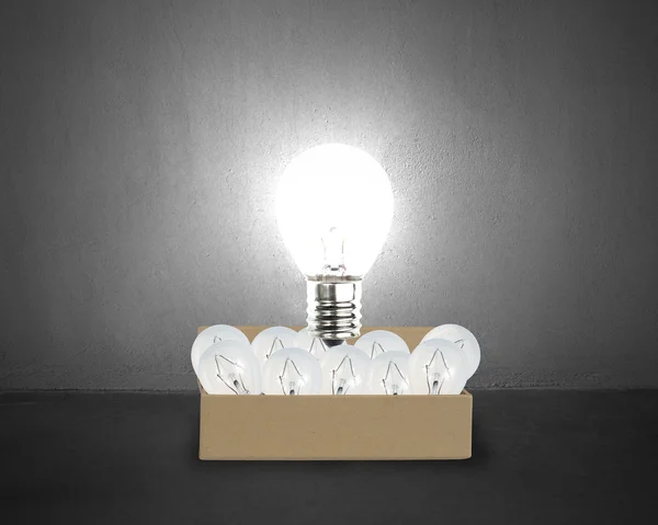 Big glowing light bulb float over opened cardboard box with many — Stock Photo, Image