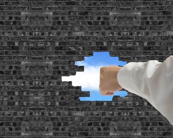 Man punching and breaking bricks wall with a big hole and blue s — Stock Photo, Image