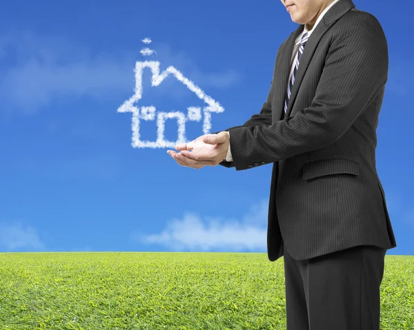 Palm opening businessman with cloud shape house in green meadow