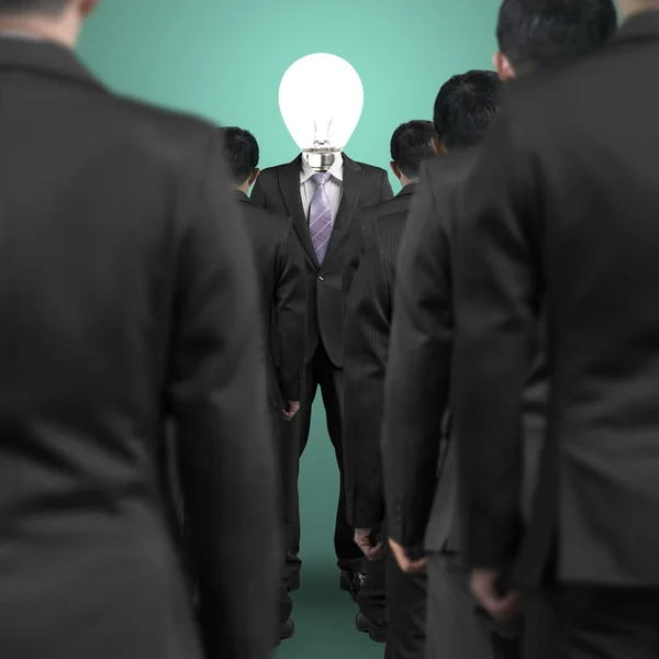 Um homem de negócios com cabeça de lâmpada em pé em frente ao gro — Fotografia de Stock