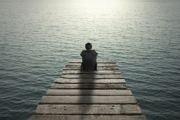 Businessman sitting and thinking on old wooden pier to the sea — Stock Photo, Image