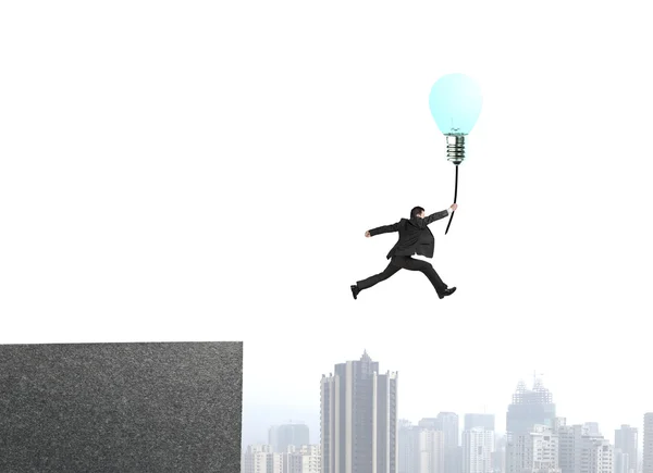 Бизнесмен прыгает с крыши здания, чтобы поймать светящийся балло лампы — стоковое фото