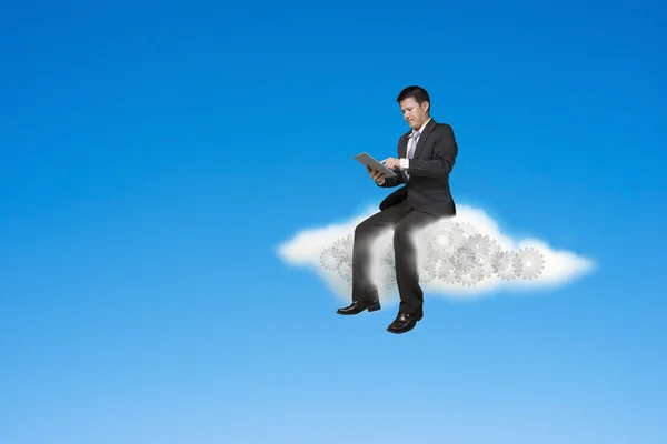Businessman using tablet and sitting on cloud with gears inside — Stock Photo, Image