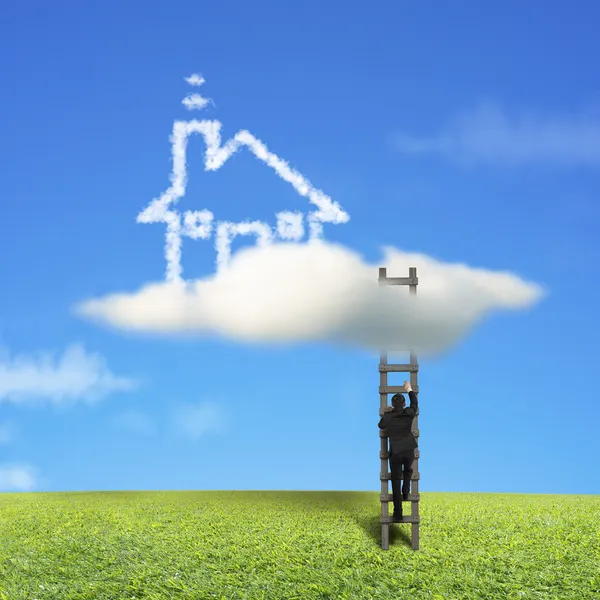 Businessman climbing on wooden ladder to reach cloud house — Stock Photo, Image