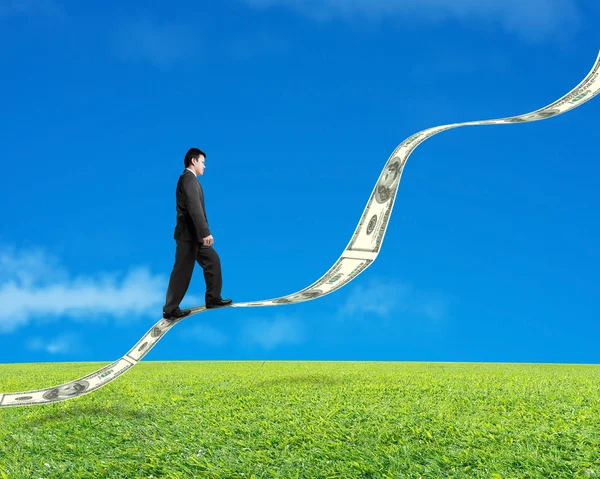 Businessman walking on growing money trend with meadow and sky — Stock Photo, Image