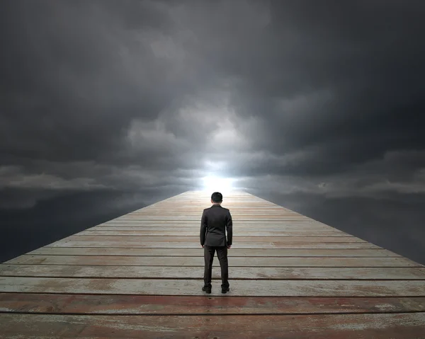Businessman standing on wooden way face sunlight with cloudy sky — Stock Photo, Image