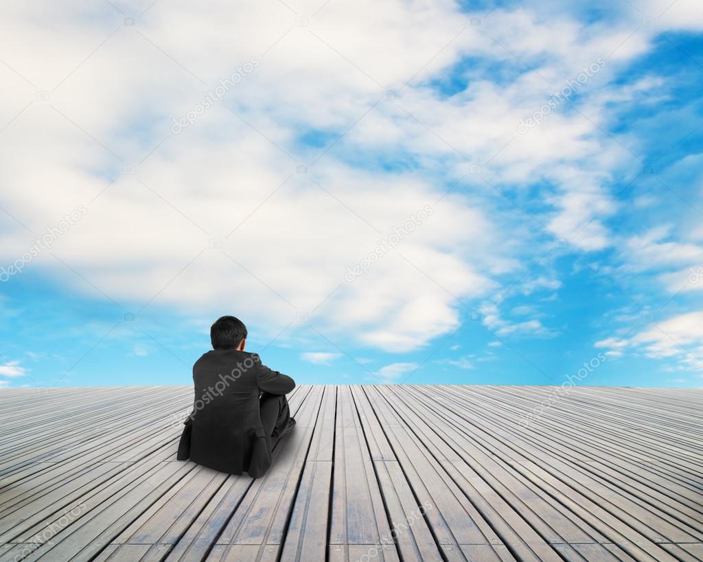 Businessman sitting on wooden floor with cloud and blue sky