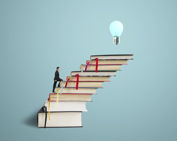 Businessman walking on stack of books with growing bulb
