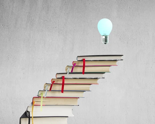 Stack of books with lamp on the top, concrete wall background — Stock Photo, Image