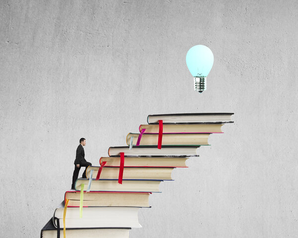 Businessman climbing on stack of books to reach top with bulb